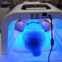Kobieta poddana zabiegowi fototerapii twarzy w salonie kosmetycznym. Urządzenie OMEGA LIGHT emituje niebieskie światło.