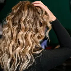 Blond włosy z falami, ułożone z pomocą aktywatora skrętu. W tle kosmetyki fryzjerskie.