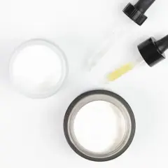 Dwa słoiczki z kremem i pipetki z serum, w tym z kwasem glikolowym, na białym tle.