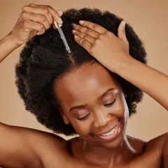 Kobieta z afro włosami aplikuje olejek na skórę głowy. Idealne olejowanie włosów średnioporowatych dla zdrowego blasku.