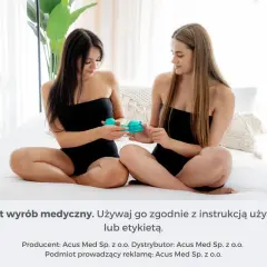 Dwie kobiety siedzą na łóżku, trzymając w dłoniach bańki chińskie. Jedna z nich pokazuje drugiej, jak wykonać masaż brzucha bańką chińską.
