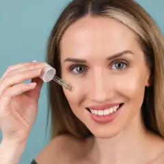 Uśmiechnięta kobieta aplikuje serum z pipetki. Czy to kwas glikolowy czy salicylowy? Skóra wygląda promiennie.