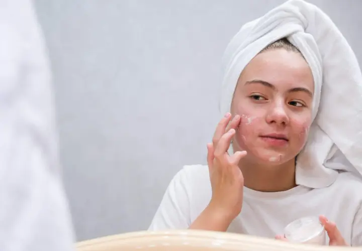 Dziewczyna z ręcznikiem na głowie aplikuje maść z witaminą A na twarz, licząc na jej pozytywne efekty w walce z niedoskonałościami.