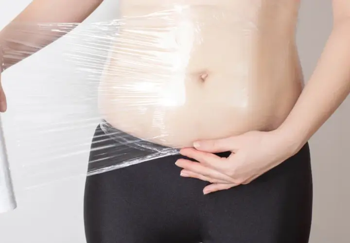 Osoba owija się folią spożywczą, przygotowując się do zabiegu body wrapping.