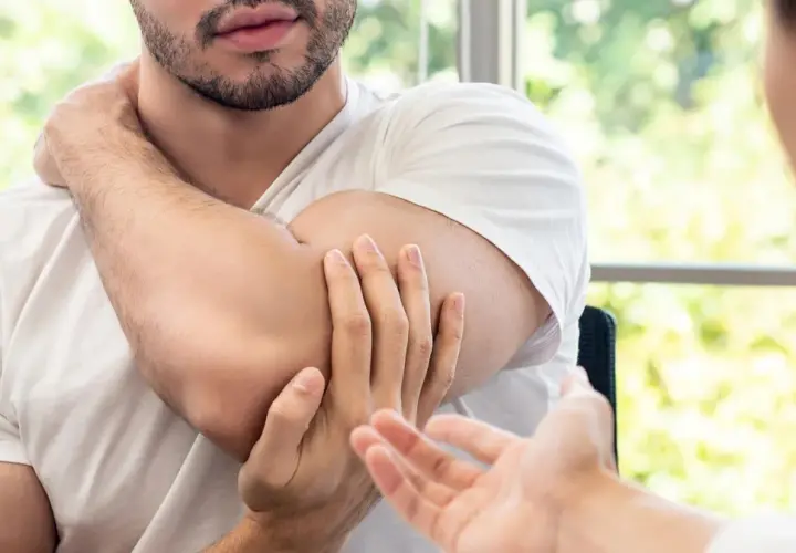 Mężczyzna masuje sobie bark, wskazując na punkty spustowe plecy. Terapeuta słucha uważnie.