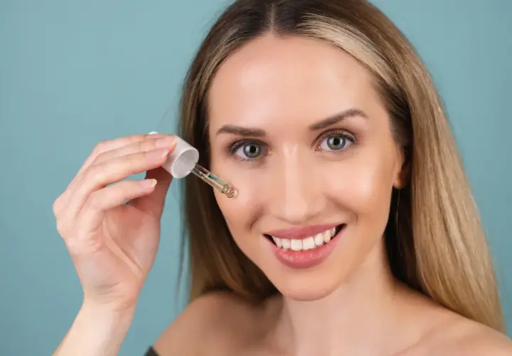 Uśmiechnięta kobieta aplikuje serum z pipetki. Czy to kwas glikolowy czy salicylowy? Skóra wygląda promiennie.