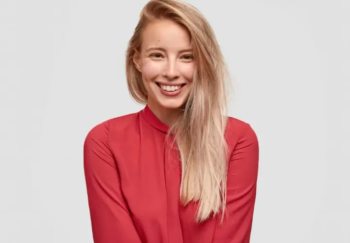 Uśmiechnięta blondynka w czerwonej bluzce. Czy toner się wyplukuje? Jej włosy są jasne i lekko potargane.