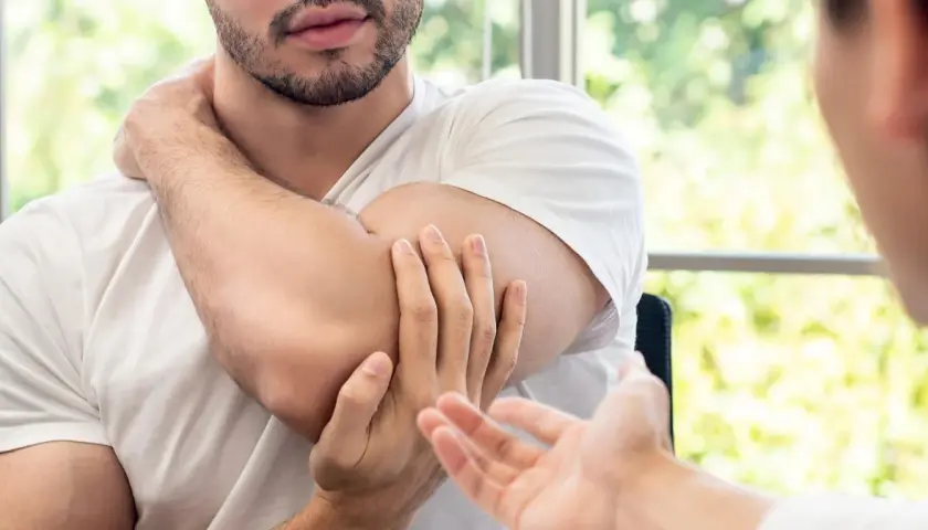 Mężczyzna masuje sobie bark, wskazując na punkty spustowe plecy. Terapeuta słucha uważnie.