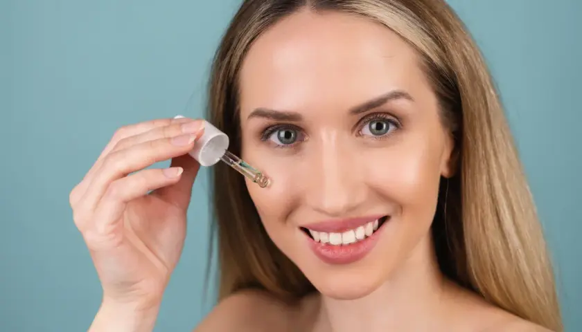 Uśmiechnięta kobieta aplikuje serum z pipetki. Czy to kwas glikolowy czy salicylowy? Skóra wygląda promiennie.