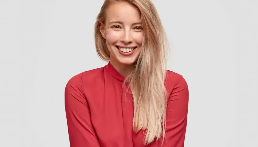 Uśmiechnięta blondynka w czerwonej bluzce. Czy toner się wyplukuje? Jej włosy są jasne i lekko potargane.