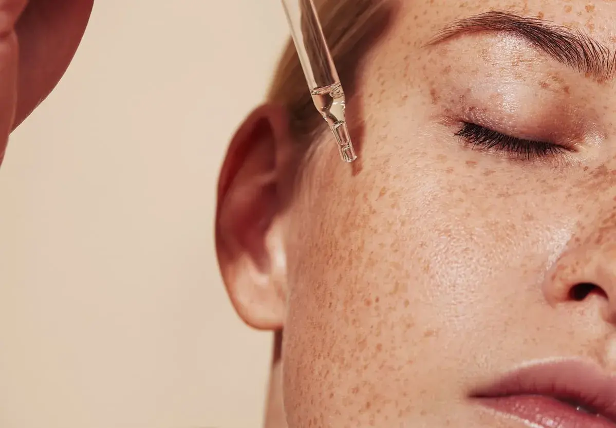 Kropla serum z pipety spada na piegowatą skórę. Dowiedz się, retinol co to i jak działa.