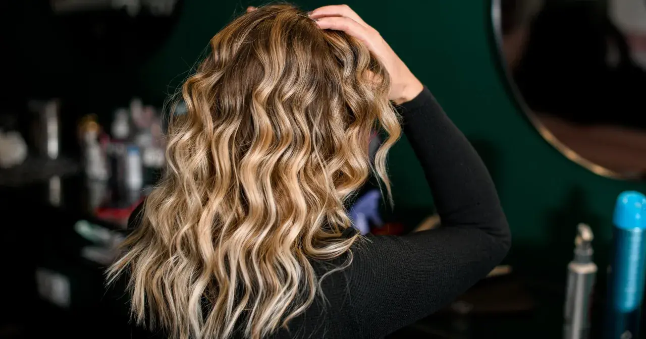 Blond włosy z falami, ułożone z pomocą aktywatora skrętu. W tle kosmetyki fryzjerskie.