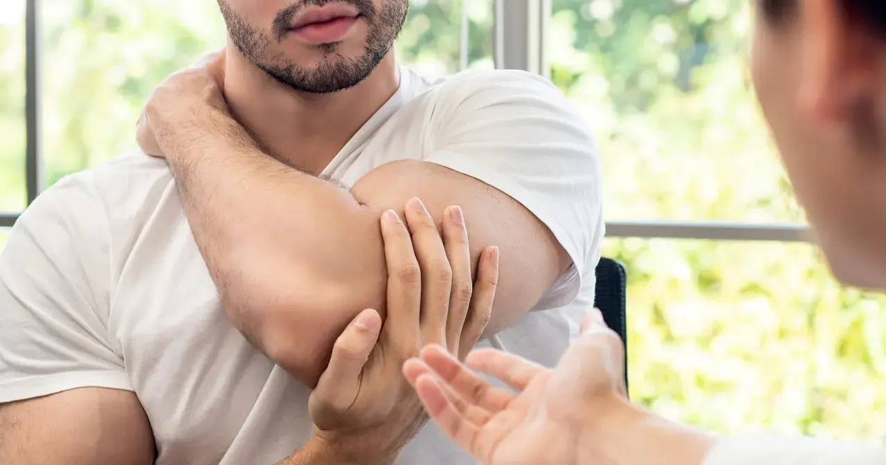 Mężczyzna masuje sobie bark, wskazując na punkty spustowe plecy. Terapeuta słucha uważnie.