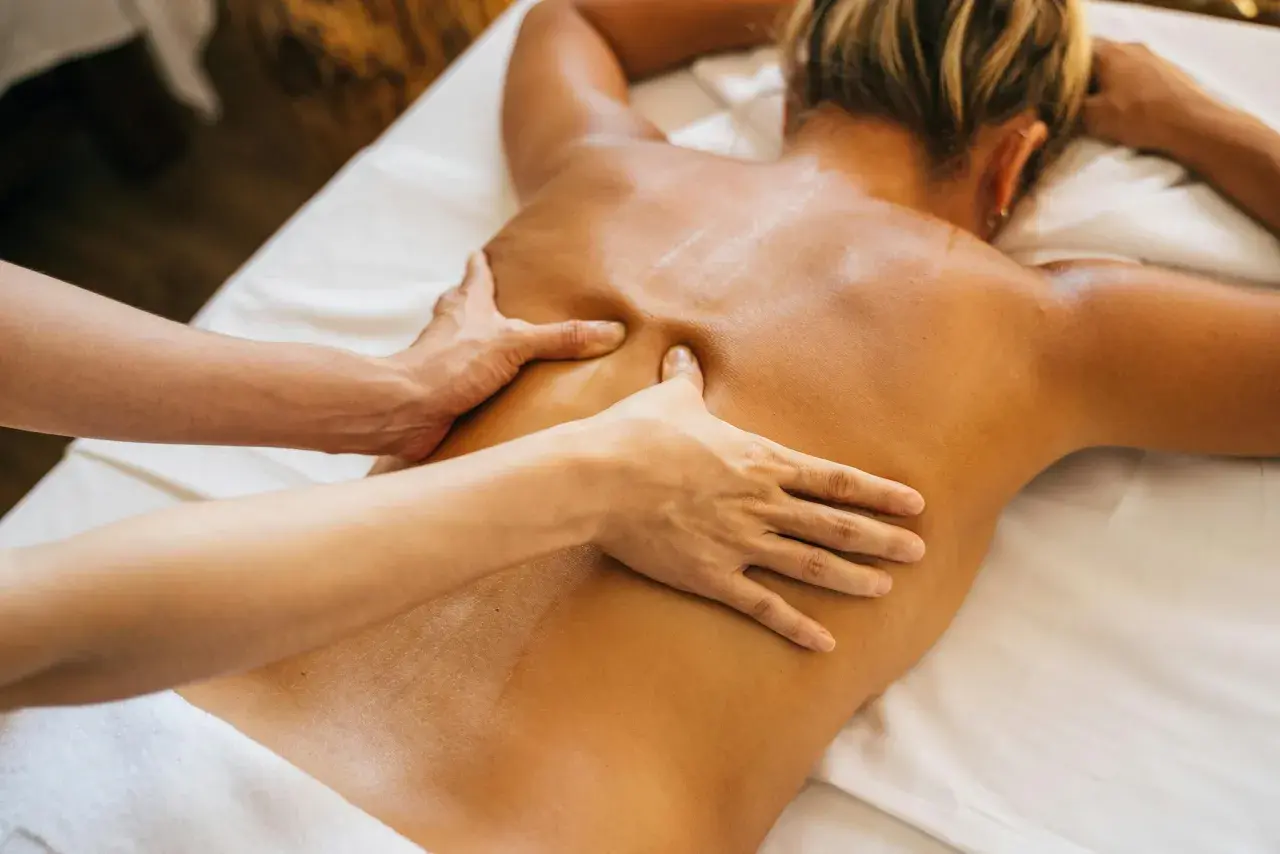 Relaks po masażu tajskim lub balijskim. Dłonie terapeuty rozluźniają napięte mięśnie pleców.