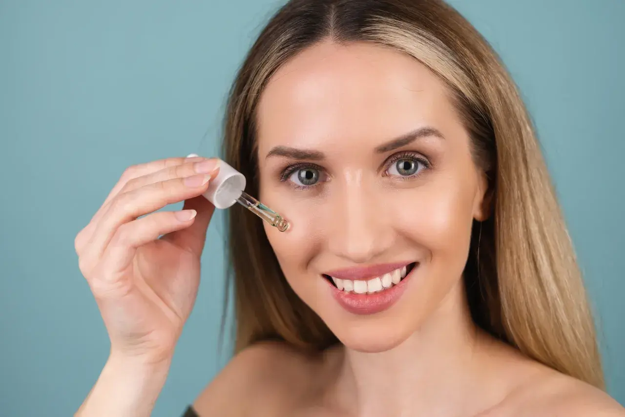 Uśmiechnięta kobieta aplikuje serum z pipetki. Czy to kwas glikolowy czy salicylowy? Skóra wygląda promiennie.